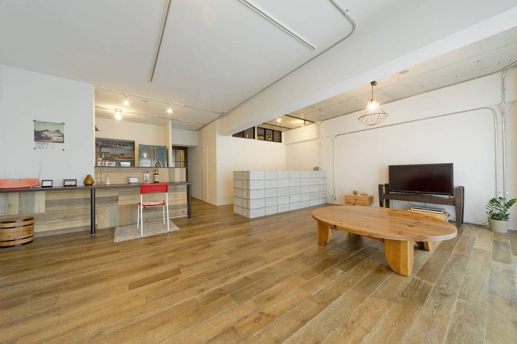 hacorenove style interior, open-plan loft living space, warm oak hardwood floors, exposed ceiling pipes, concrete block partition, low wooden oval table, industrial pendant light, white walls, minimalist Japanese-industrial atmosphere