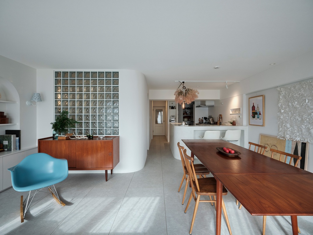 hacorenove style interior, open-plan living dining room, mid-century walnut furniture, blue rocker chair, glass block wall, white walls, gray tile floor, warm natural light, eclectic modern atmosphere