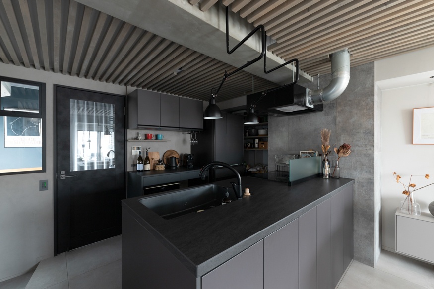 hacorenove style interior, industrial modern kitchen, matte black cabinetry, dark countertop, exposed wooden slat ceiling, concrete walls, metal ductwork, black pendant lights, moody monochromatic palette, minimalist Japanese industrial aesthetic