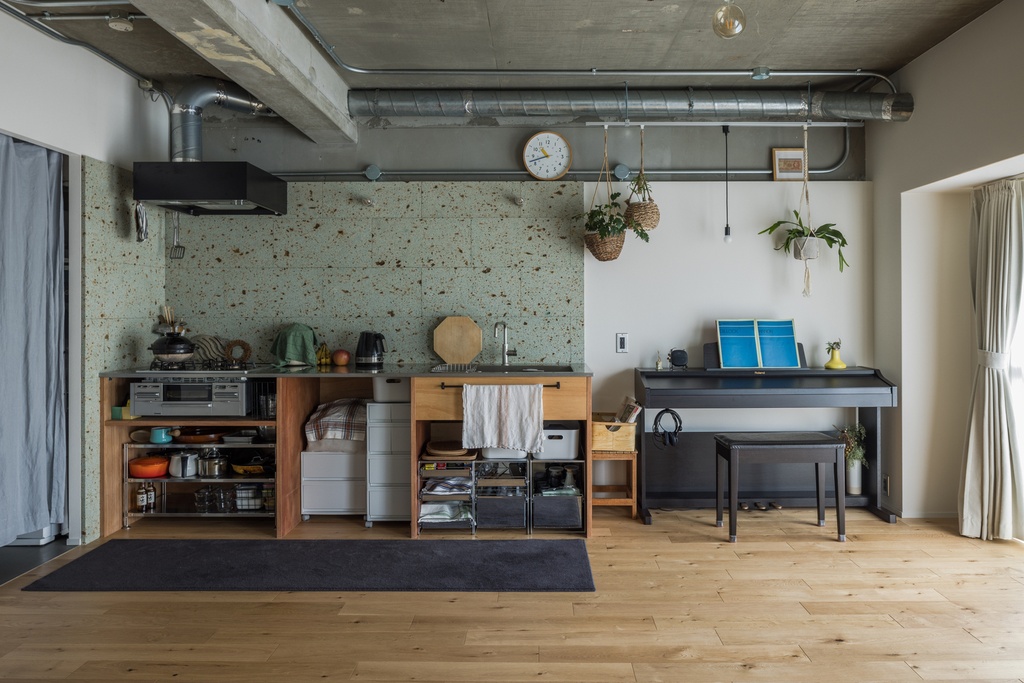 hacorenove style interior, industrial loft kitchen, exposed concrete ceiling, metal ductwork, green terrazzo backsplash, open wood shelving, light oak flooring, hanging plants, warm lived-in atmosphere