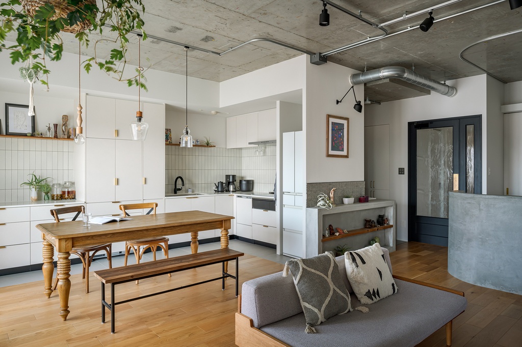 hacorenove style interior, open-plan kitchen-living space, exposed concrete ceiling, industrial ductwork, white cabinetry, oak hardwood floors, hanging greenery, glass pendants, warm natural light, Japanese industrial-organic aesthetic