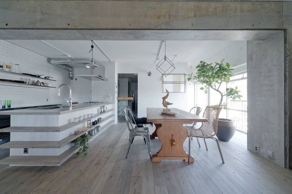 hacorenove style interior, open-plan kitchen dining, exposed concrete beams and columns, white subway tile backsplash, light oak wood flooring, industrial pendant lights, exposed pipes, indoor tree, natural light, minimalist Japanese industrial aesthetic