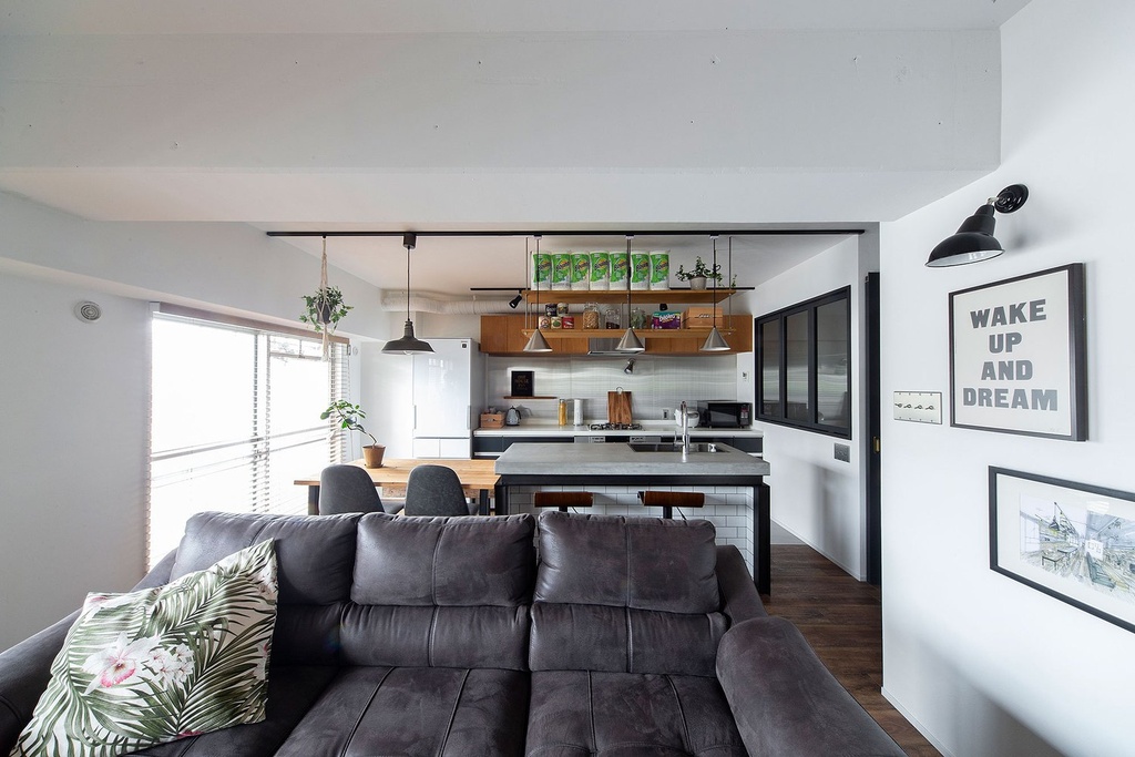 hacorenove style interior, open-plan living kitchen, white walls, dark wood flooring, concrete countertop, subway tile island, industrial pendant lights, suspended wood shelving, gray sofa, natural light, casual urban atmosphere