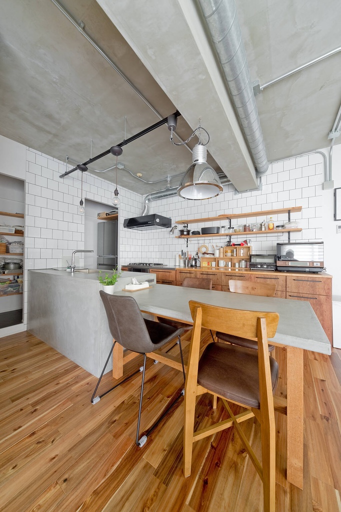 hacorenove style interior, industrial loft kitchen, exposed concrete ceiling, white subway tile backsplash, warm wood flooring, concrete island counter, open wood shelving, metal pendant lights, exposed ductwork, natural light